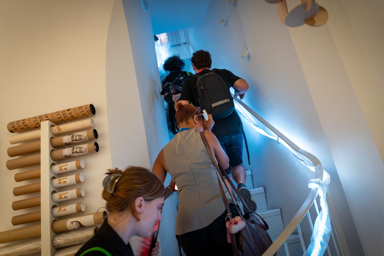 Visitors climb a narrow stairwell lit by a strip of white light wound along the handrail